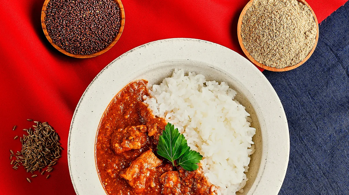 テーブルの中央に置かれたカレーがあり、そのまわりに複数のスパイスが置かれている